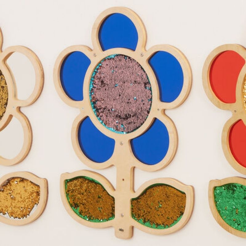 TTS blue Mark Making Sequin Daisy Frame mounted on wall showing complete flower shape with sequin surface and acrylic mirror petals - tactile sensory wall panel