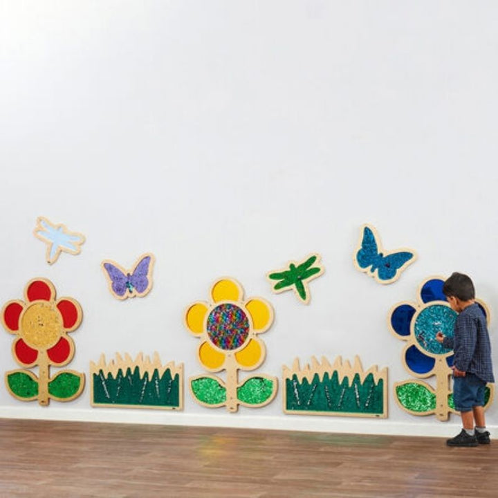 Child actively exploring the TTS blue sequin daisy frame mounted on wall, demonstrating tactile sensory wall panel engagement and fine motor skill development