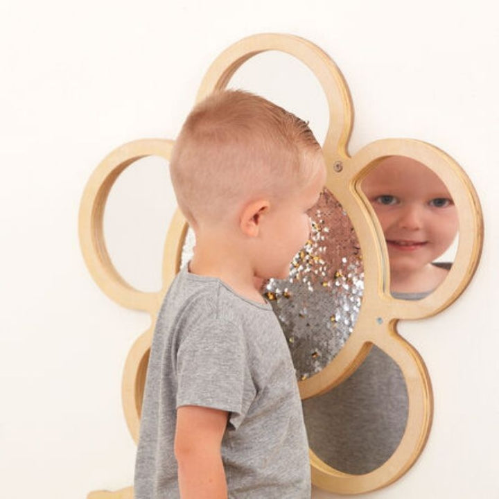 Child gazing into mirror petals of TTS Mark Making Sequin Daisy Frame, demonstrating self-awareness and communication development through interactive sensory wall panel