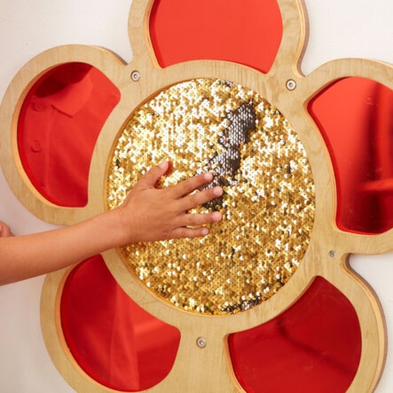 Close-up of hand stroking TTS red sequin daisy frame petals, showing reversible mermaid sequin surface and mirror detail - tactile wall panel for therapy rooms