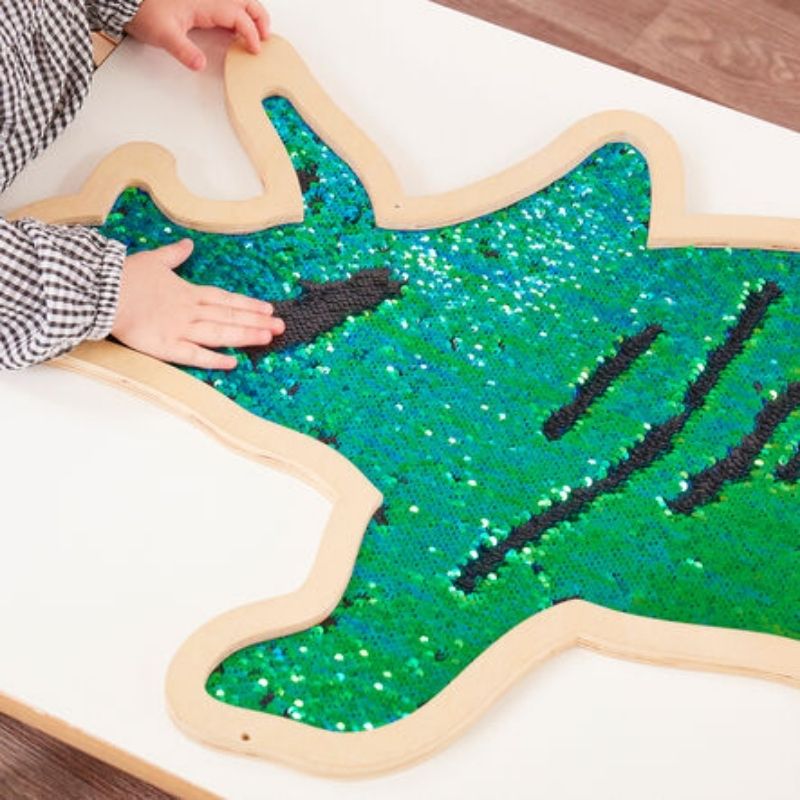 Child playing with the TTS Mark Making Sequin Giant Dinosaurs tactile wall panel on a table, swiping colourful flip sequins for sensory exploration