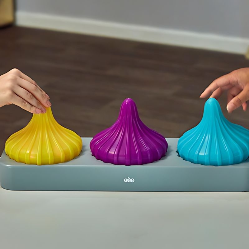 TTS Light Up Spinning Tops set of three in yellow, purple, and blue resting on the rechargeable docking station, showing the included charging base for classroom and home use
