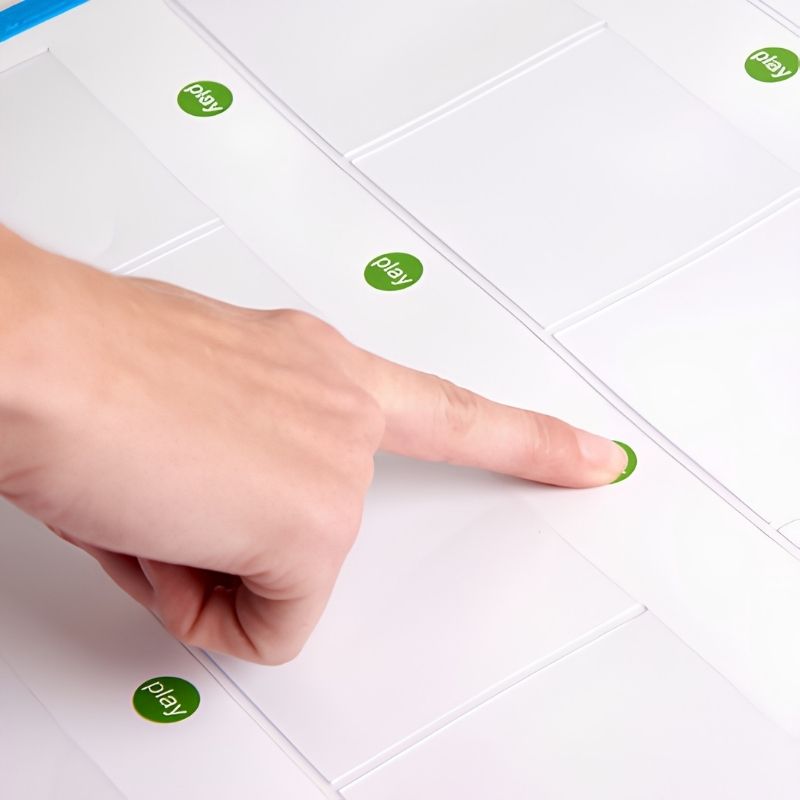 Close-up of a finger pressing a green play button on the TTS Interactive Talking Mat, demonstrating the simple one-touch recording and playback interaction