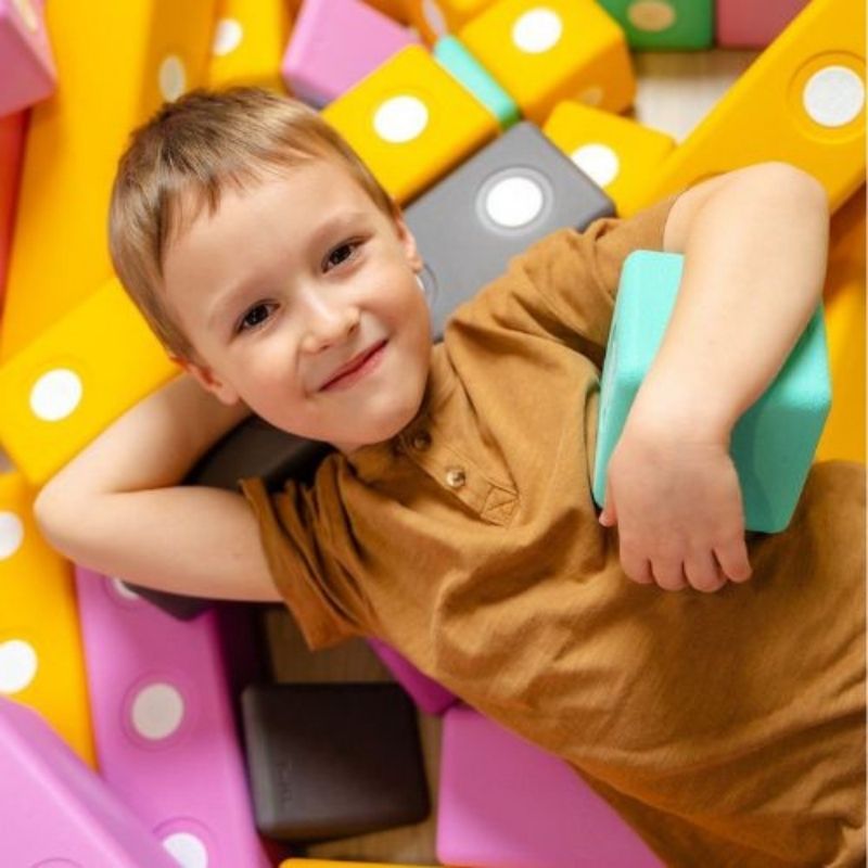 Boy actively building a floor-scale structure with the TUKI BIG Magnetic Blocks Builder 110, showing the whole-body gross motor engagement and large-format 10cm foam block construction the 110-piece largest BIG BUILDER group set enables
