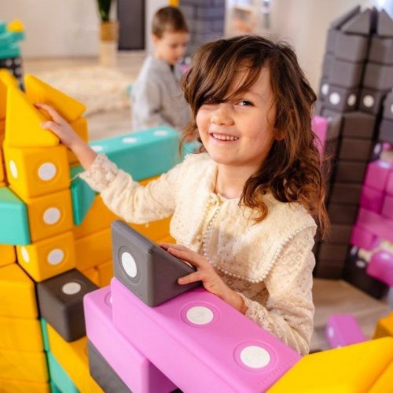 Top view of child actively building with the TUKI BIG Magnetic Blocks Builder 12, showing the large-format 10cm foam block floor construction in use for gross motor and spatial reasoning development