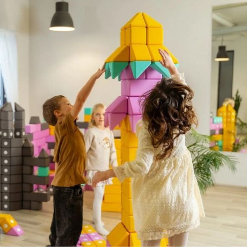 Three children simultaneously building floor-scale structures with the TUKI BIG Magnetic Blocks Builder 128, showing the large-group sub-building dynamic that 128 large-format 10cm magnetic foam blocks enables for groups of 7-10 children