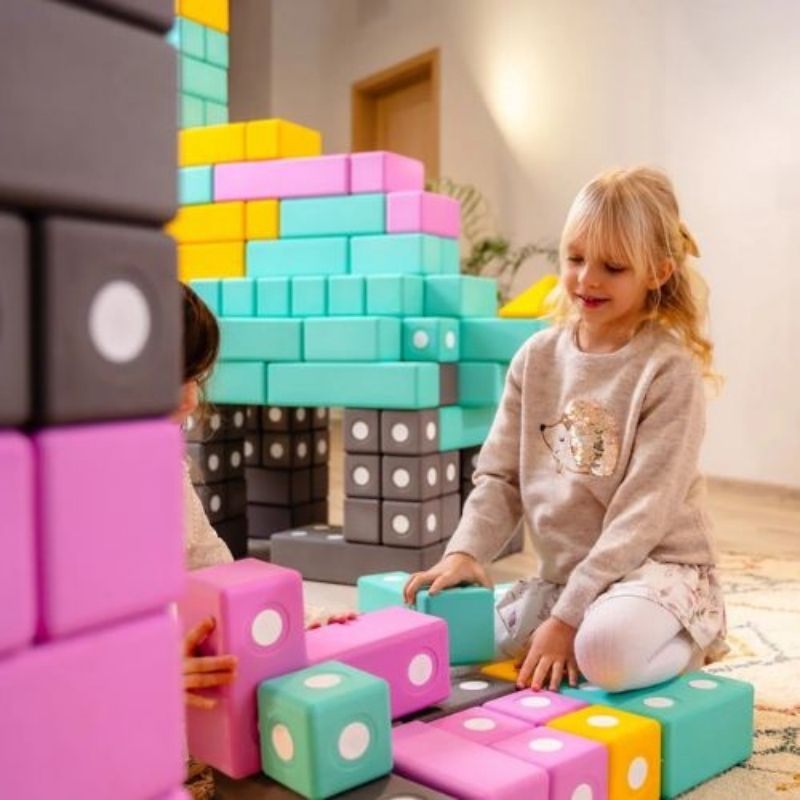 Two children actively building a floor-scale structure with the TUKI BIG Magnetic Blocks Builder 128, showing the collaborative large-format 10cm foam block construction the 128-piece largest BUILDER group set supports