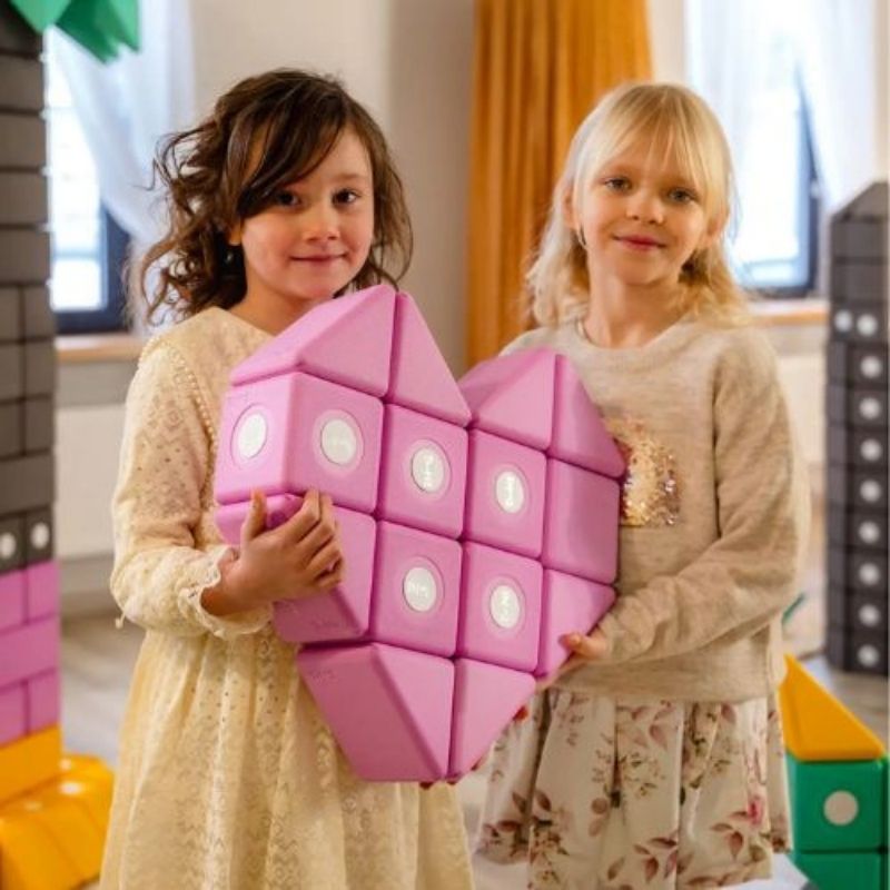 Two girls building a heart shape together with TUKI Big Magnetic Foam Blocks Smart 280, demonstrating collaborative sensory play and social communication development