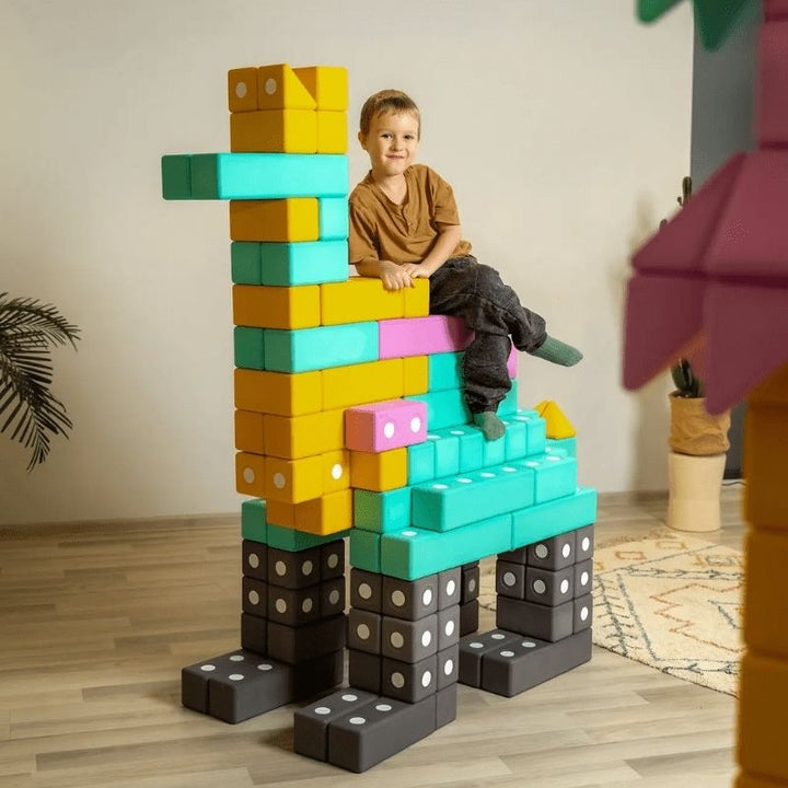 Child actively playing on top of a floor-scale structure built with the TUKI BIG Smart Magnetic Blocks Smart 100, showing the architectural floor-build scale that 100 large-format magnetic foam blocks in 4 Smart shapes enables