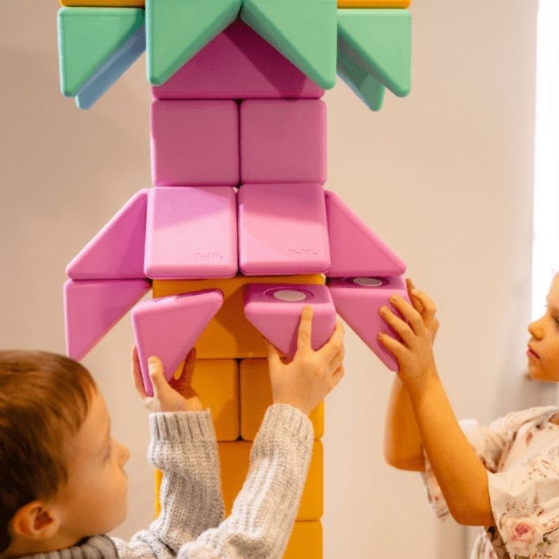 Two children building a floor-scale structure with the TUKI BIG Smart Magnetic Blocks Smart 100, demonstrating the paired sub-group construction the 100-piece 4 Smart TUKI shapes enable within a group of 6-9 children