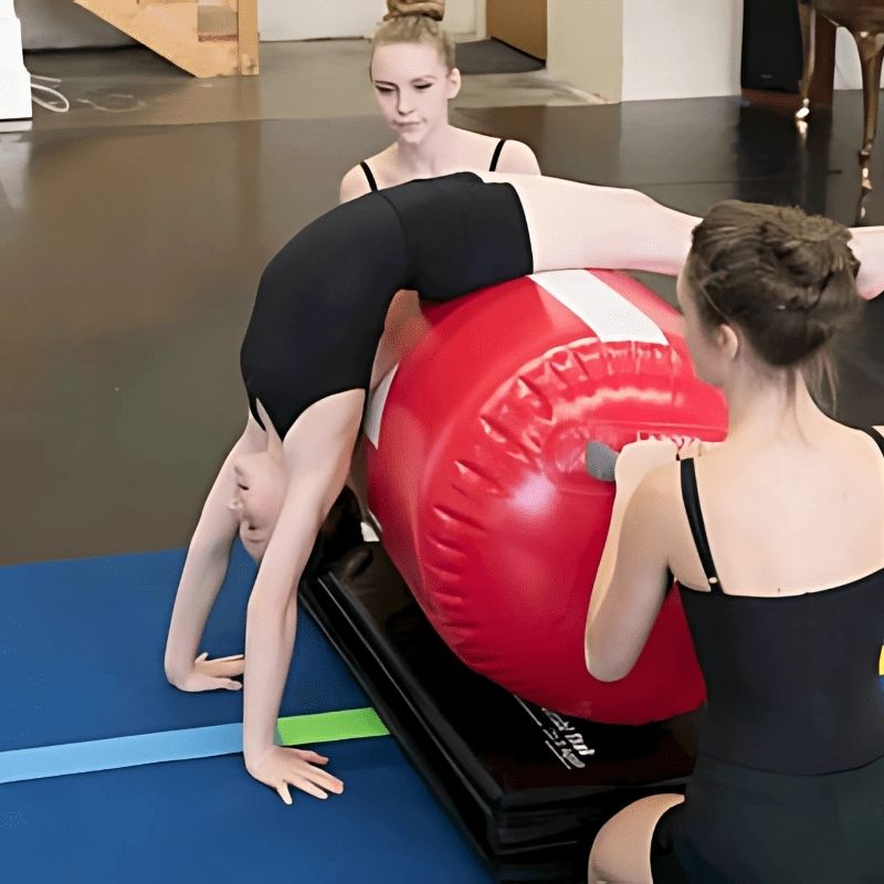 Three girls actively training on Tumbl Trak Air Barrels in a gymnastics class setting, showing multiple simultaneous stations and the portable inflatable barrel roller in recreational and skill training use