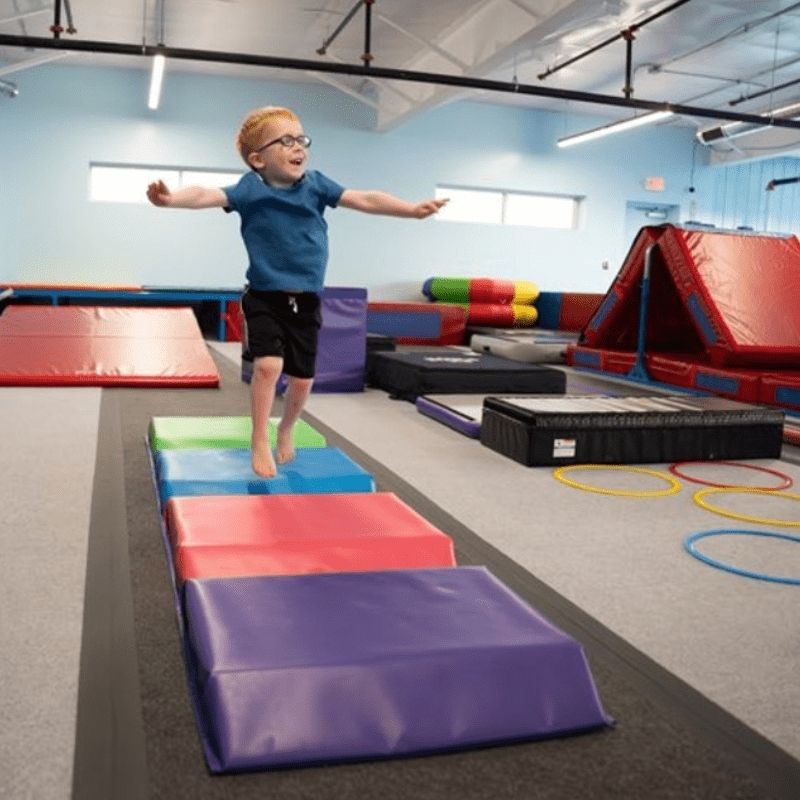 Child actively playing on the Tumbl Trak Color Tunnel Mat in an indoor setting, demonstrating jumping, stepping, and movement exploration across the bright four-panel foam path for gross motor and sensory development