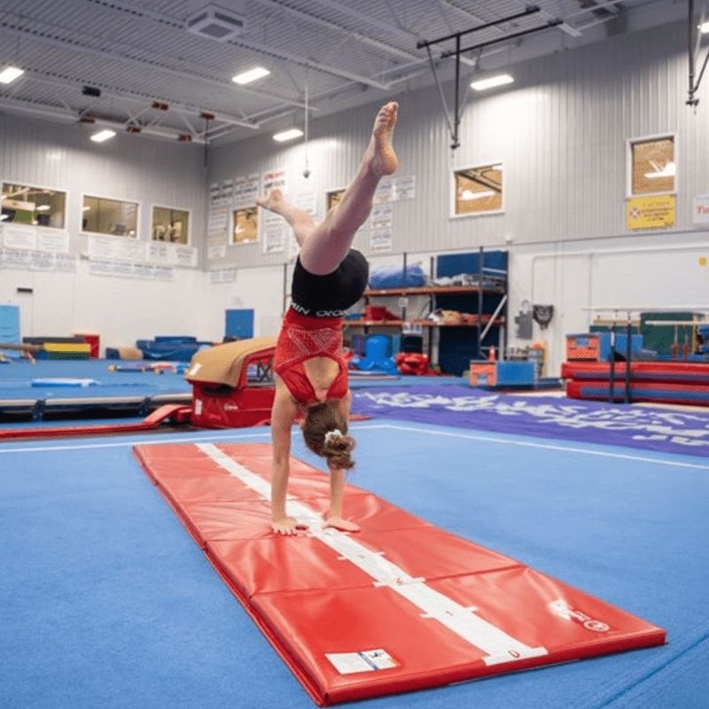 Young gymnast performing a handstand on the Tumbl Trak Hopscotch Beam Mat beam stripe side in a gymnasium, demonstrating balance beam practice and straight-line gymnastics skill training on the 3x12ft floor mat