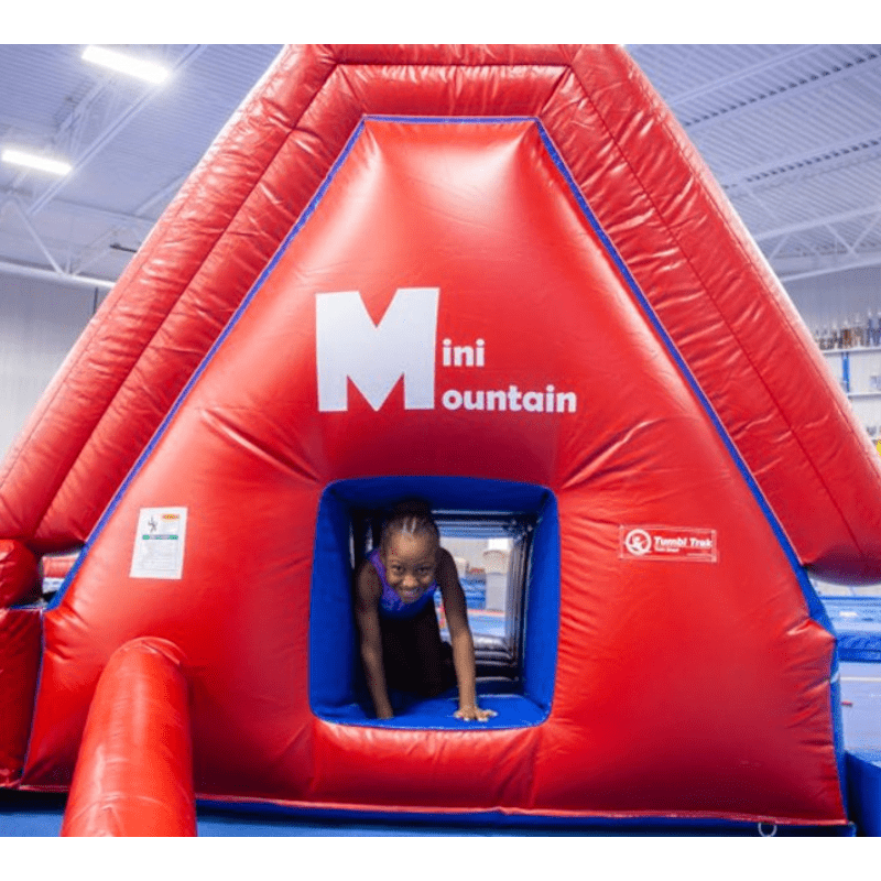 Child actively crawling through the built-in tunnel of the Tumbl Trak Mini Mountain inflatable gymnasium play station, demonstrating the tunneling activity of the Four Fun Groups and motor planning development