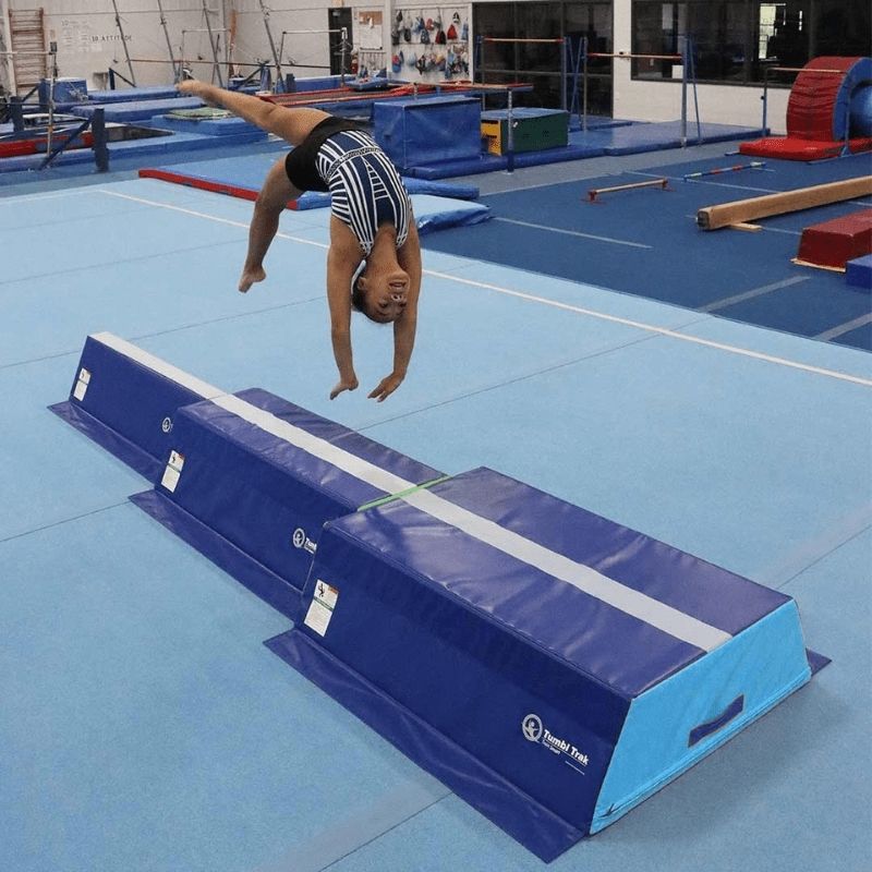 Gymnast performing a back flip on the Tumbl Trak Pyramid Beam Blocks stacked trapezoid configuration, demonstrating the firm foam surface and elevated beam station used for gymnastics skill development and balance beam training progressions