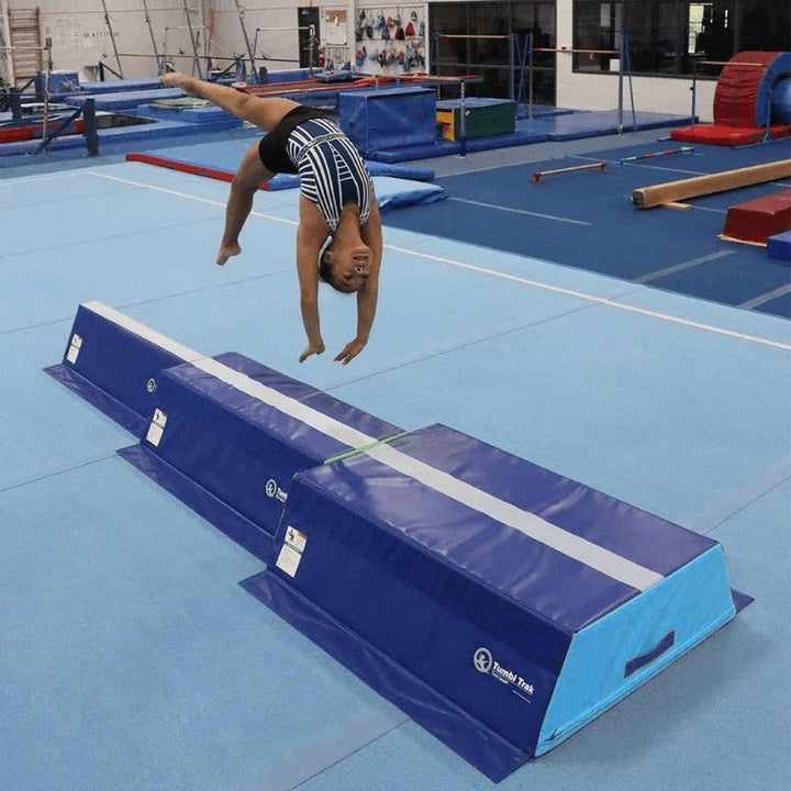 Gymnast performing a back flip on the Tumbl Trak Pyramid Beam Blocks stacked trapezoid configuration, demonstrating the firm foam surface and elevated beam station used for gymnastics skill development and balance beam training progressions