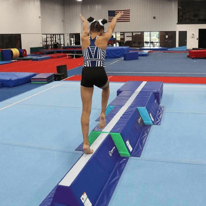 Back view of a girl balancing on the Tumbl Trak Pyramid Beam Blocks, showing the white centre line visual guide and wide-to-narrow surface that builds postural control, proprioceptive awareness, and beam confidence for beginner and intermediate gymnasts