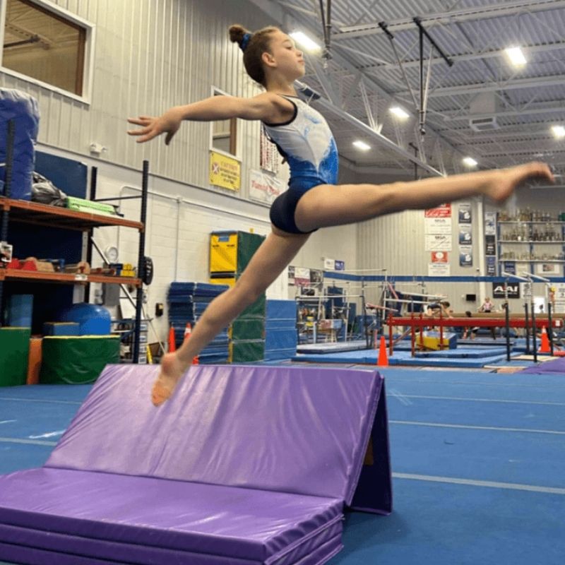 Girl actively jumping or tumbling on the Tumbl Trak Rebound Mat, demonstrating the springier dual-layer foam that provides extra lift and more forgiving landings for advanced gymnastics tumbling skills and cheer training