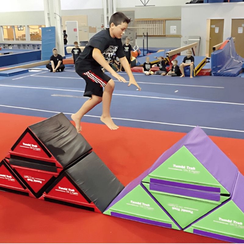 Children actively playing on the Tumbl Trak Slanted Ninja Steps in an indoor gymnasium setting, showing the configurable foam ninja obstacle steps in use for agility and motor planning development