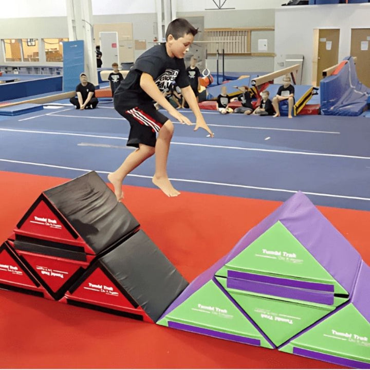 Children actively playing on the Tumbl Trak Slanted Ninja Steps in an indoor gymnasium setting, showing the configurable foam ninja obstacle steps in use for agility and motor planning development