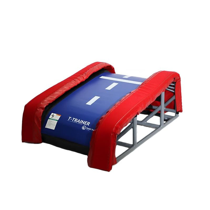 Tumbl Trak T-Trainer gymnastics vault training device showing the blue vinyl tramp bed surface with red padded bolsters and grey steel spring frame, a versatile vault and bar training aid for gyms across North America