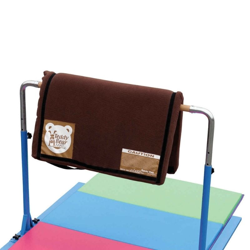 Tumbl Trak Teddy Bear Mat draped over a gymnastics bar or railing showing the flexible light-density foam construction used as instant bar padding and equipment cushioning in gymnastics clubs and home play spaces