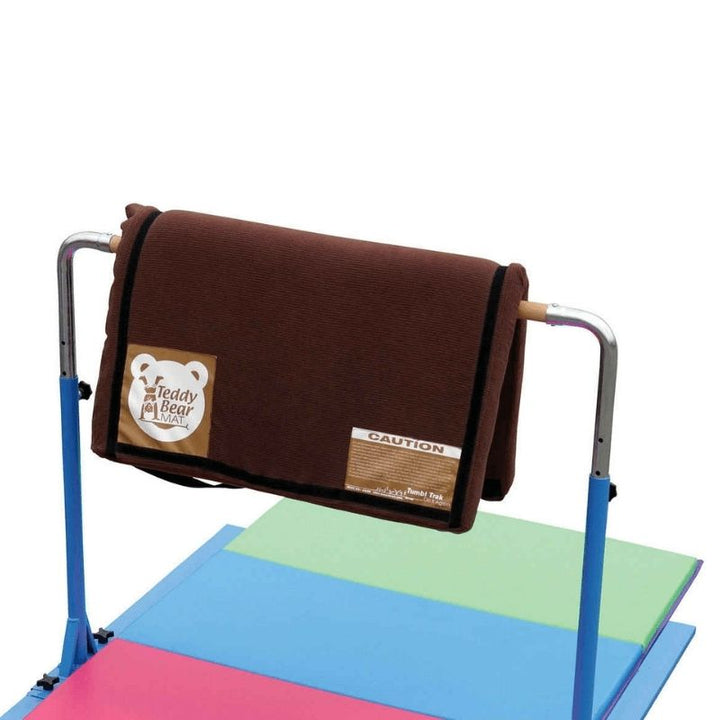 Tumbl Trak Teddy Bear Mat draped over a gymnastics bar or railing showing the flexible light-density foam construction used as instant bar padding and equipment cushioning in gymnastics clubs and home play spaces