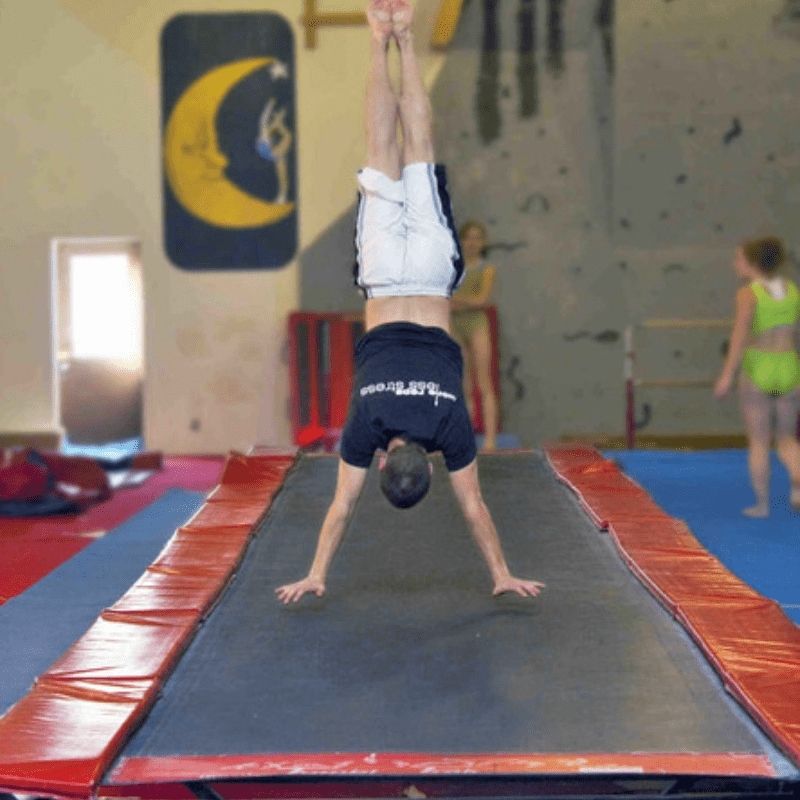 Young male gymnast performing a handstand on the Tumbl Trak tumbling track, showing the gymnastics trampoline track in active use for training and proprioceptive skill building