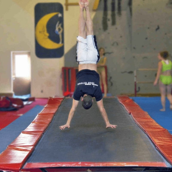 Young male gymnast performing a handstand on the Tumbl Trak tumbling track, showing the gymnastics trampoline track in active use for training and proprioceptive skill building