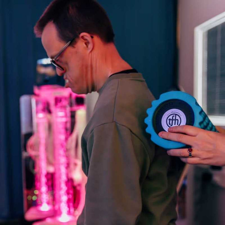 Man using the TFH Big Texture Vibrating Roller on his shoulder for deep pressure massage and proprioceptive input in a therapy setting