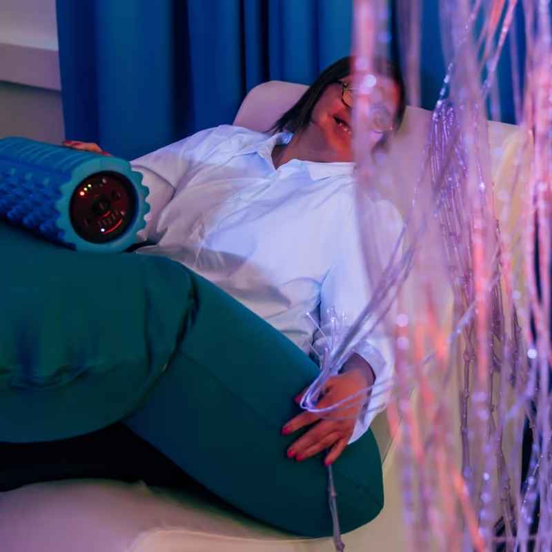 Woman resting in a sensory room with the TFH Big Texture Vibrating Roller, illustrating calming deep pressure input from this vibrating roller