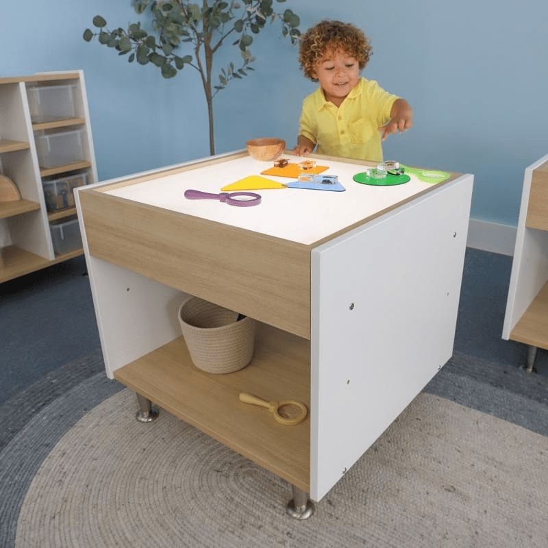 Child engaged with the Whitney Brothers elevatED Adjustable Light Table, showing the illuminated LED surface and the contemporary two-tone white and textured white oak design at active play height
