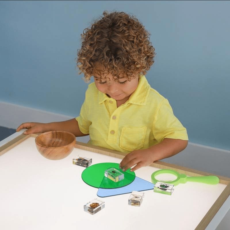 Close-up of a child placing objects on the Whitney Brothers elevatED Adjustable Light Table, showing the bright evenly distributed LED surface and the brushed nickel legs