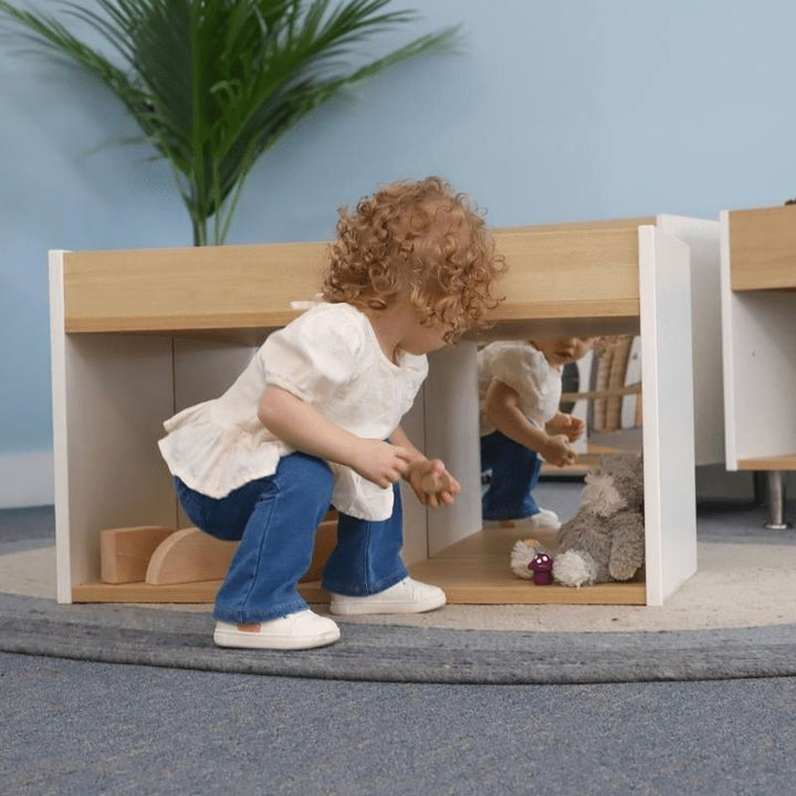 Toddler actively playing with the Whitney Brothers elevatED I-See-Me Toddler Mirror Cabinet, showing the pull-to-stand mirror experience and the contemporary white oak elevatED Collection design