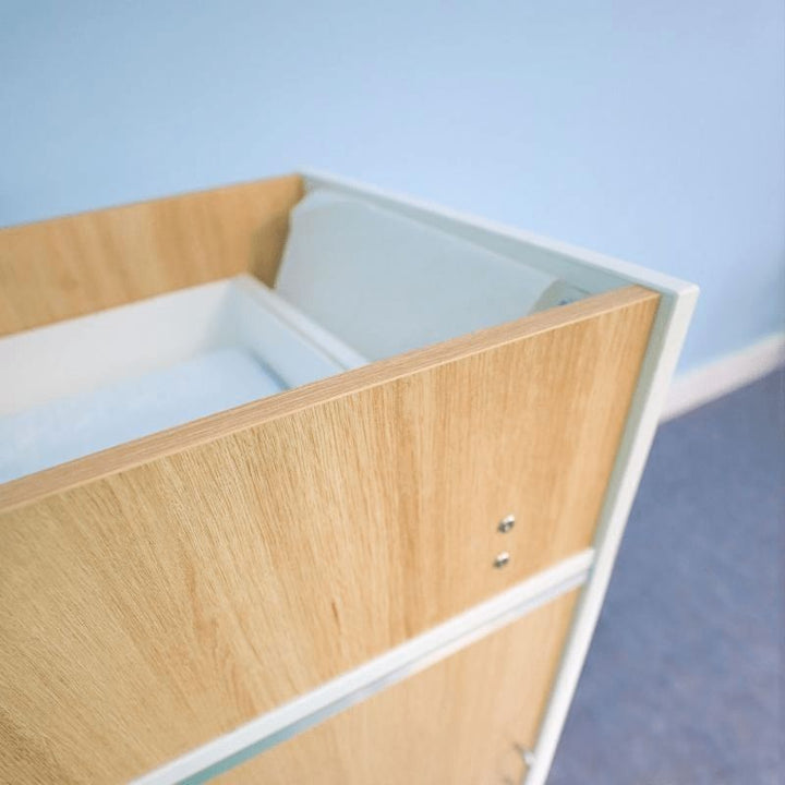 Close-up corner view of the Whitney Brothers elevatED Infant Changing Cabinet showing the professional-grade edge banding, thermofused melamine construction, and brushed nickel leg detail