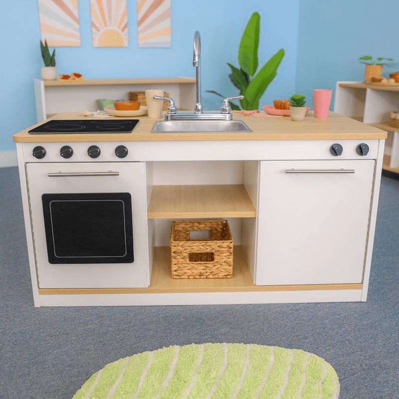 Whitney Brothers elevatED Kitchen Island Breakfast Bar in a classroom or play space showing the full front kitchen face with stovetop, sink, oven, dishwasher, and open centre shelves