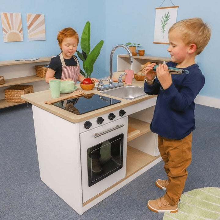 Two children playing at the Whitney Brothers elevatED Kitchen Island Breakfast Bar, showing the 360-degree collaborative design with one child cooking and one at the breakfast bar