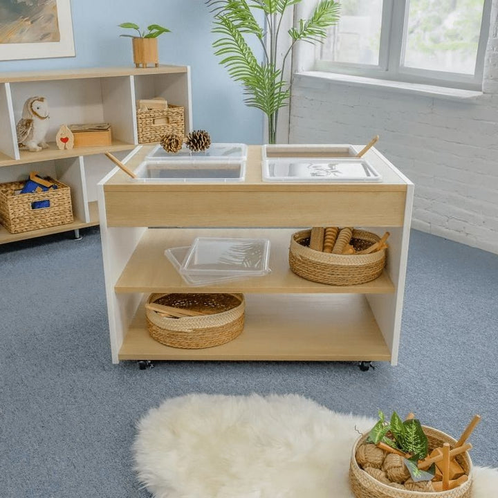 Full indoor view of the Whitney Brothers elevatED Mobile Sensory Table in a classroom setting, showing the four-tray STEM and sensory play surface and the heavy-duty lockable casters