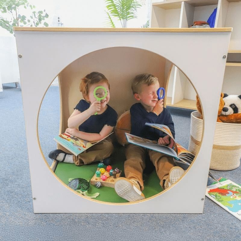 Child inside the Whitney Brothers elevatED Play House Cube with Floor Mat, showing the 25-inch circular opening, the custom-fitted vinyl floor mat, and the warm white and birch panel design