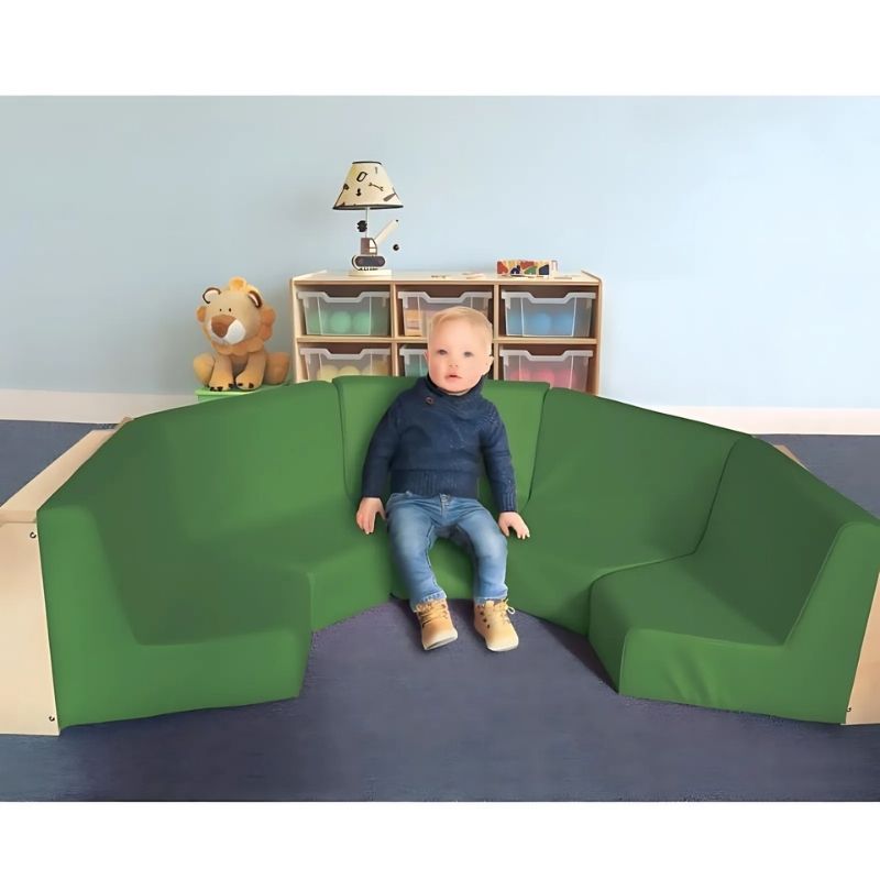 Child seated comfortably in the Whitney Brothers Five Section Reading Nook, showing the green vinyl padded seat and backrest of the configurable classroom reading seating
