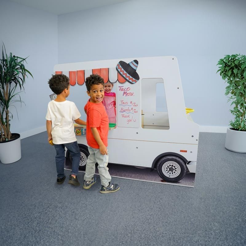 Two children at the side-panel serving counter of the Whitney Brothers Imagination Truck role play vehicle, showing the customer interaction zone of the dramatic play truck