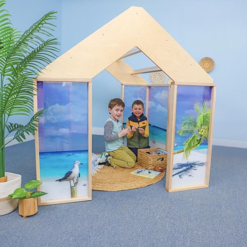 Two children inside the Whitney Brothers Nature View Play Beach House, showing the immersive ocean beach scene printed on the shatterproof acrylic panels and the open pergola-style roof
