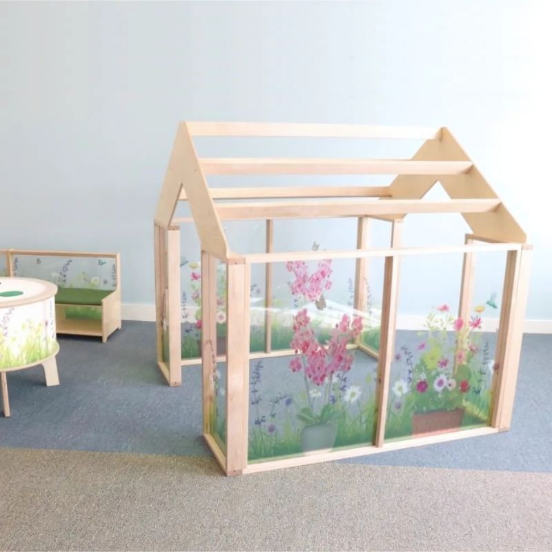 Side view of the Whitney Brothers Nature View Play Greenhouse showing the shatterproof acrylic panels printed with wildflower fields and the open pergola-style roof for air circulation and visibility