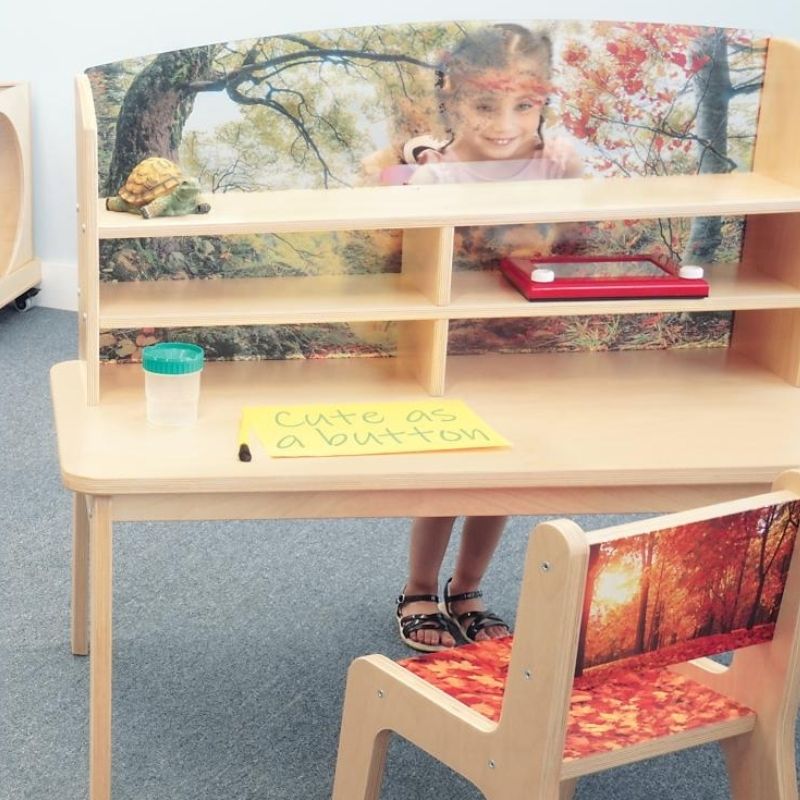 Child leaning on the Whitney Brothers Nature View Writing Center showing the full desk surface, forest scene acrylic panel, and the 42.5" wide birch plywood work area