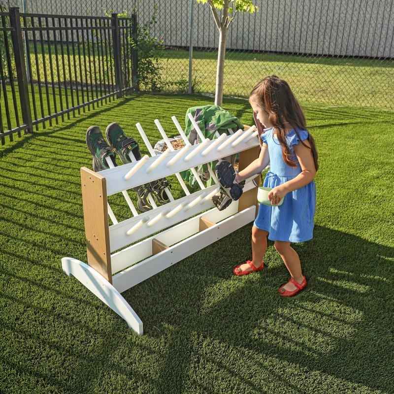 Child independently hanging outdoor footwear on the Whitney Brothers outdoorED Boot Rinse Rack, showing child-accessible open base design and weatherproof HDPE construction