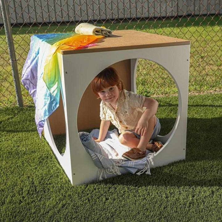 Child sitting inside the Whitney Brothers outdoorED Play House Cube in an outdoor classroom setting, showing quiet retreat space with three circular openings and polar white HDPE construction