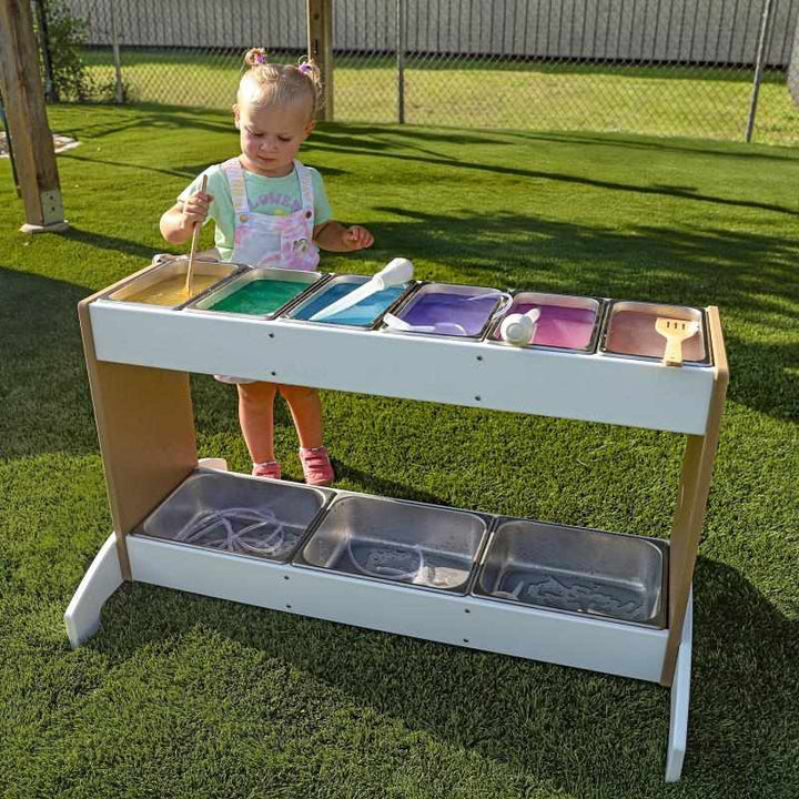 Girl actively mixing materials at the Whitney Brothers outdoorED Potion Station outdoors, showing nine interchangeable stainless steel trays in use for outdoor STEM sensory play