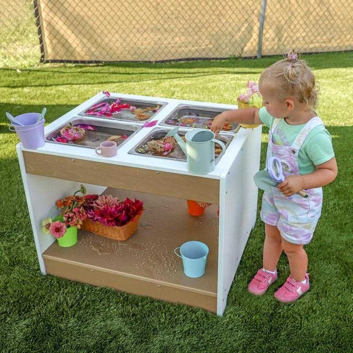 Landscape view of child engaged in outdoor sensory play at the Whitney Brothers outdoorED Sensory Table, showing full weatherproof HDPE profile in outdoor classroom setting