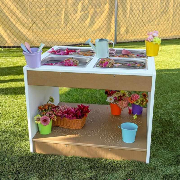 Whitney Brothers outdoorED outdoor sensory table front view styled with flowers in an outdoor classroom setting, showing textured woodgrain maple and polar white HDPE finish
