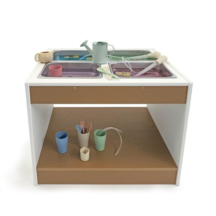 Whitney Brothers outdoorED Sensory Table front view with sensory materials and toys arranged across four stainless steel trays, showing table in active outdoor learning use